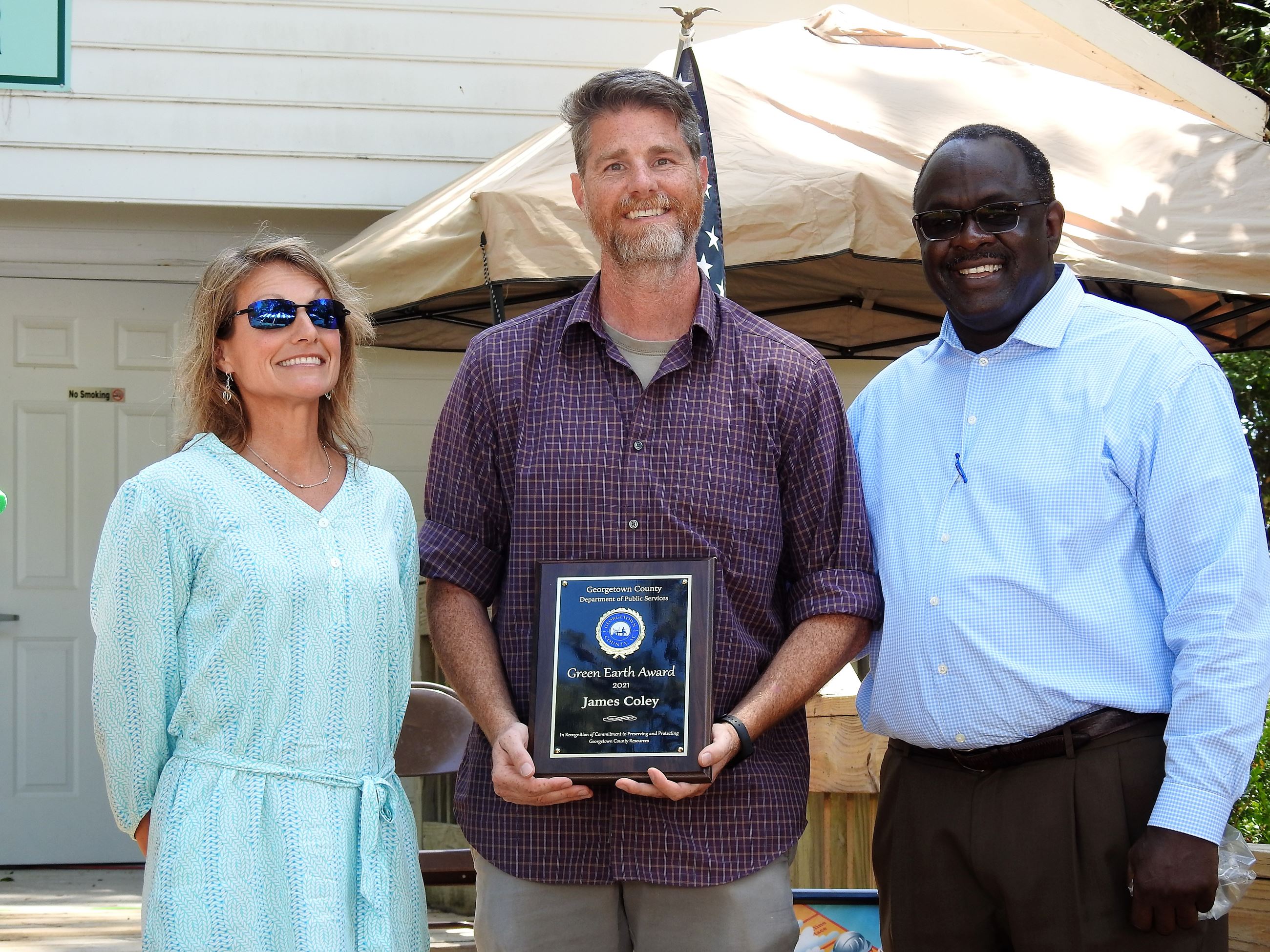James Coley holding award plaque with a colleague standing on each side