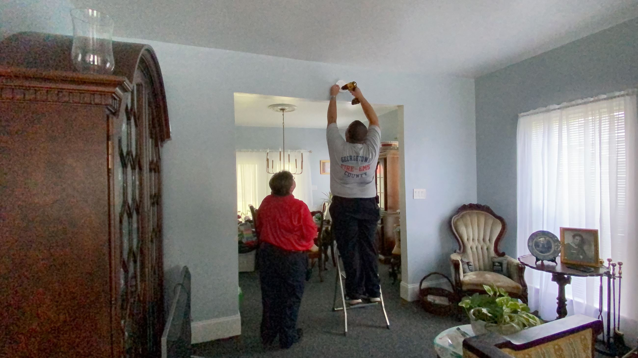 A firefighter stands on a ladder to install a home smoke detector.