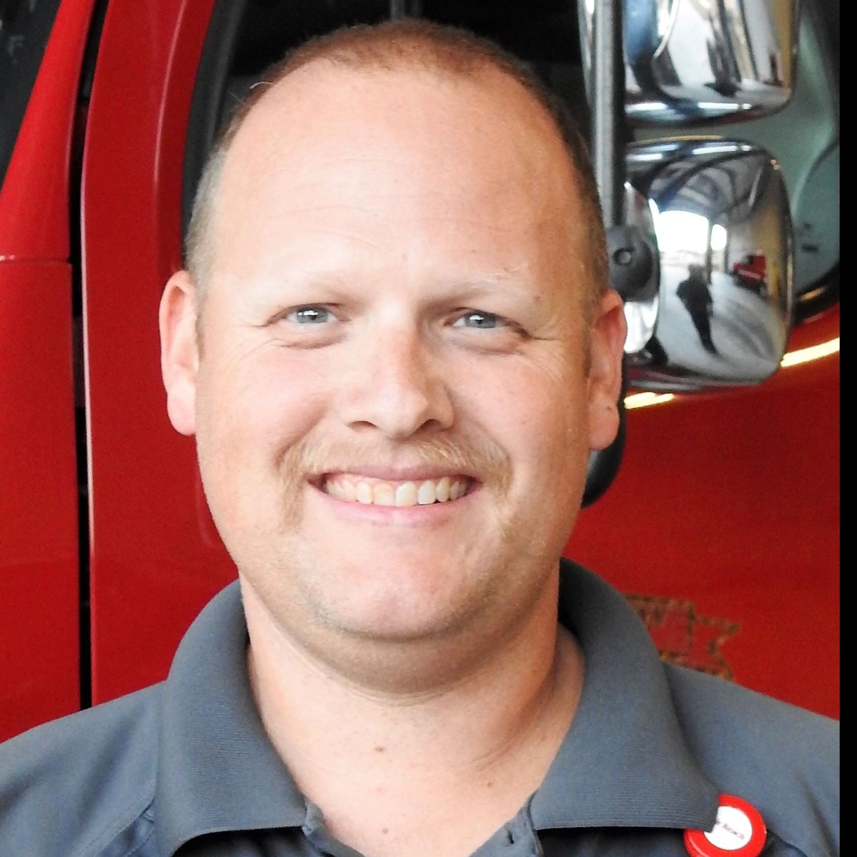 Picture of Lt. Dale Hewitt in a uniform shirt in front of a fire truck.