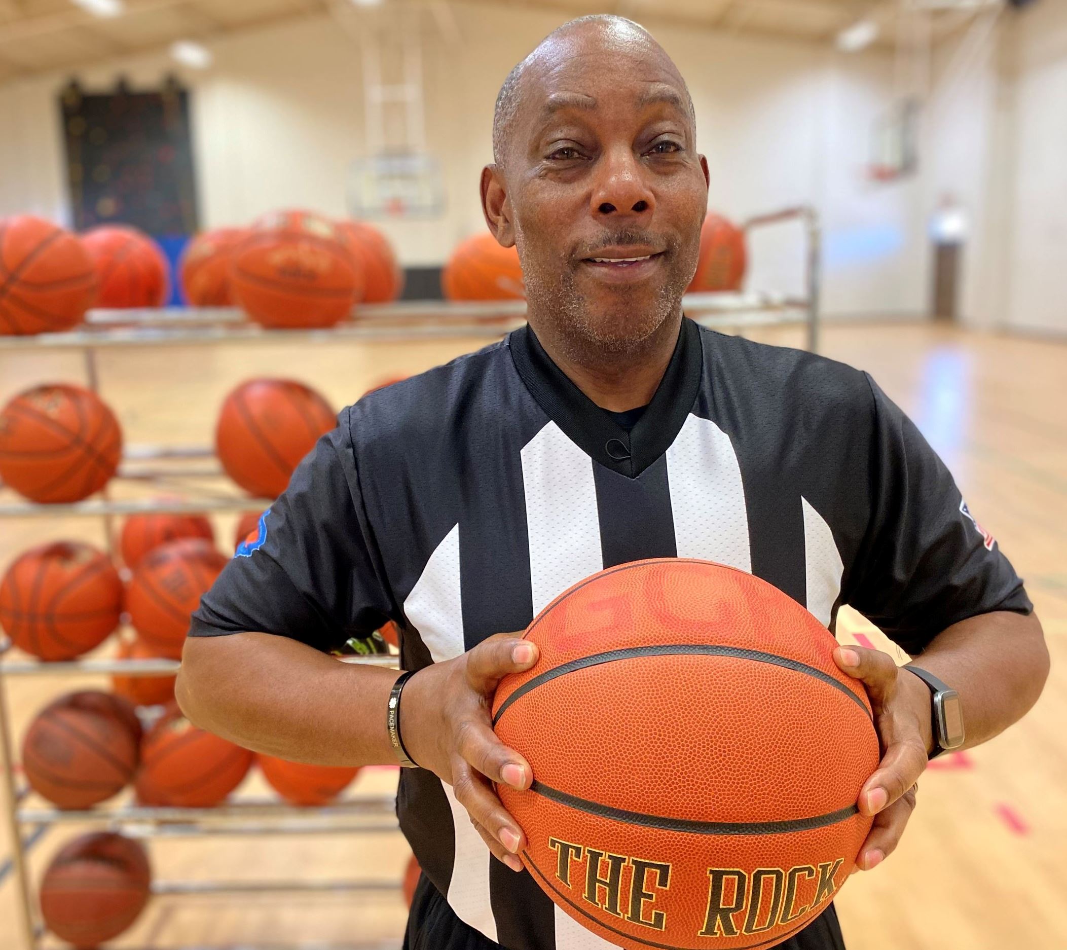 Joey Manigault is pictured in a gym in his officials uniform holding a basketball.