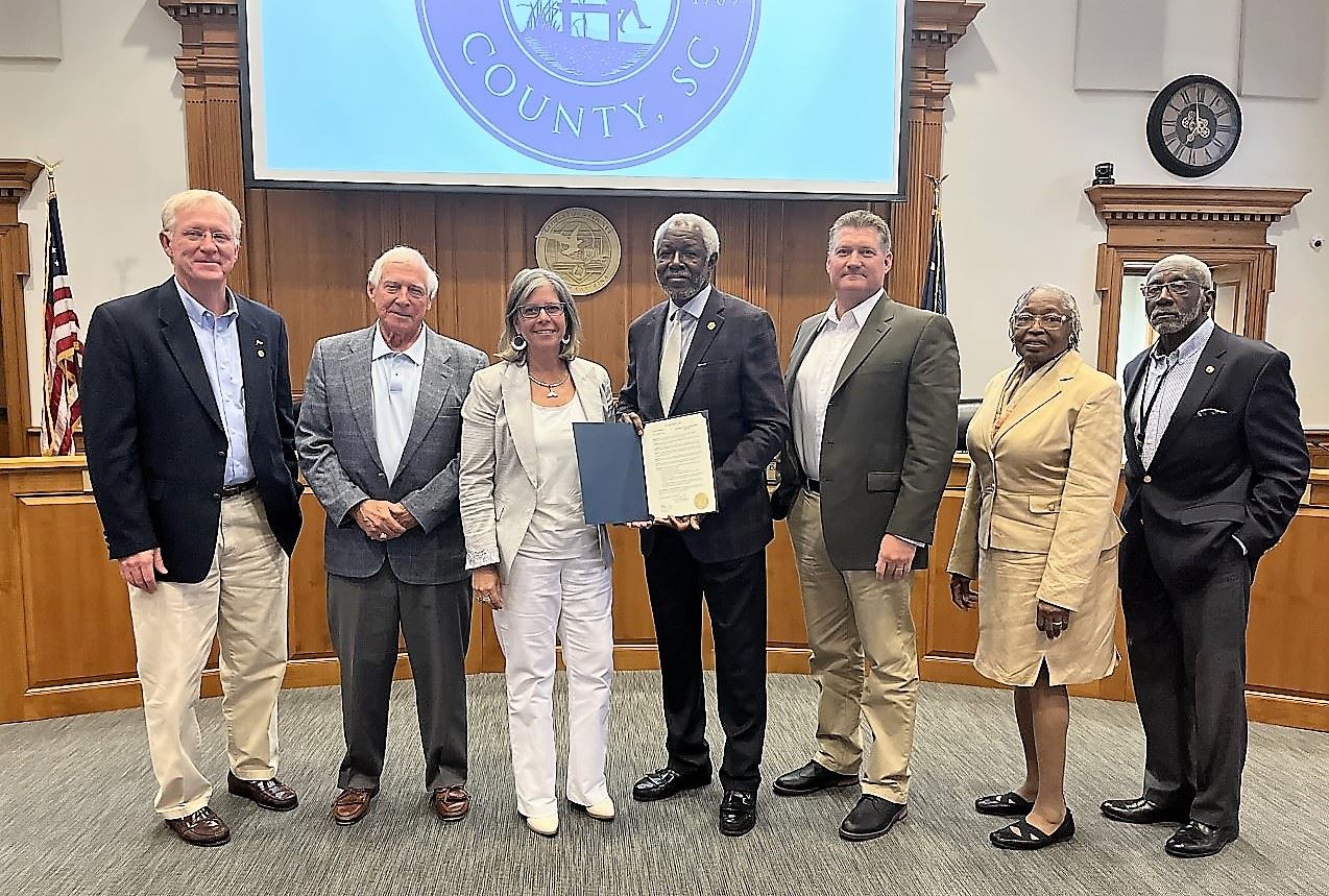 County Council Members stand in a row, holding a framed proclamation
