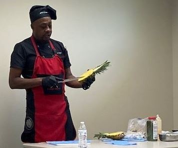 A chef holds a knife while preparing a pineapple dish.