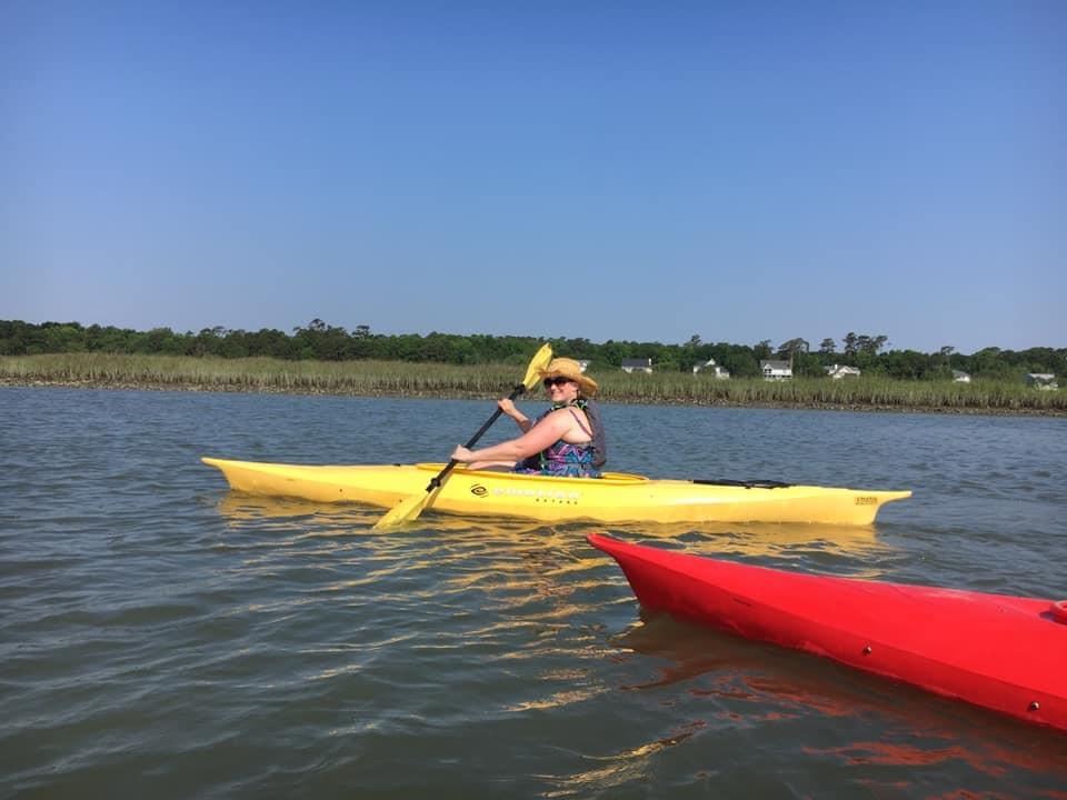 A woman paddles along the creek in a yellow kayak