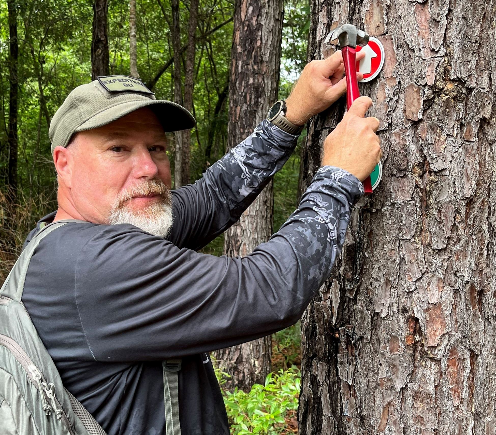 TL Staub hammers a trail marker into a tree in Rocky Point Community Forest