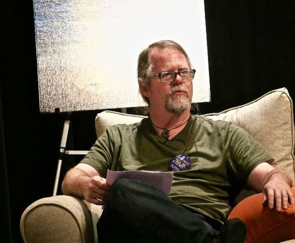 Tim Conroy speaks from a seated position in an armchair during a relaxed presentation