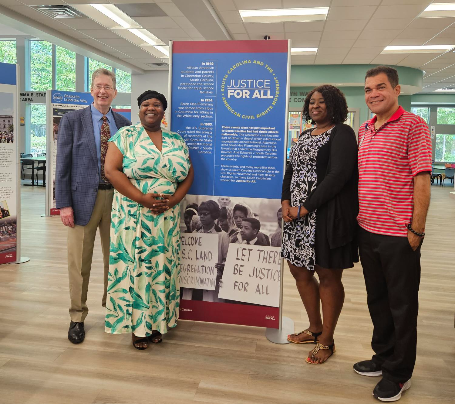 Two men and two women pose smiling in front of a banner that is part of the exhibit