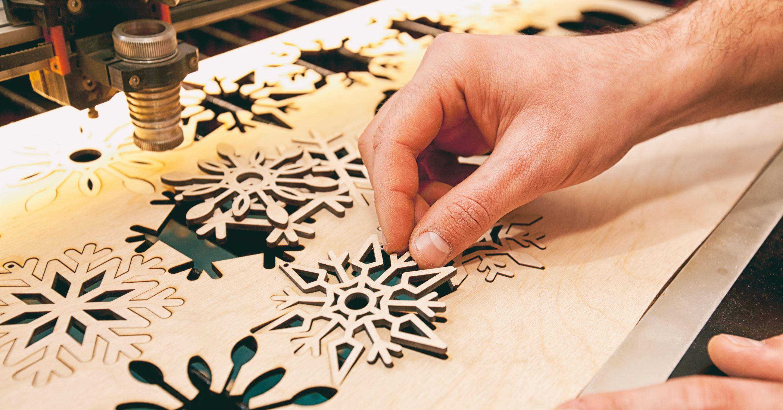 closeup of a hand removing a snowflake lasercut from a piece of wood.