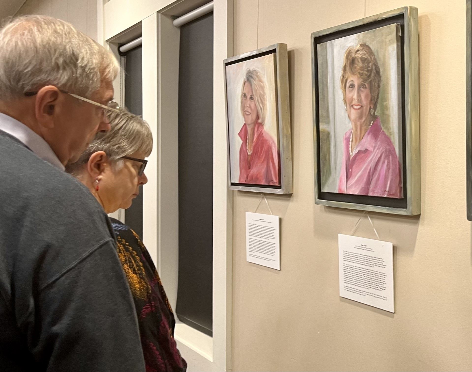 A man and a woman look at a portrait of Jean Cross on display in the library auditorium