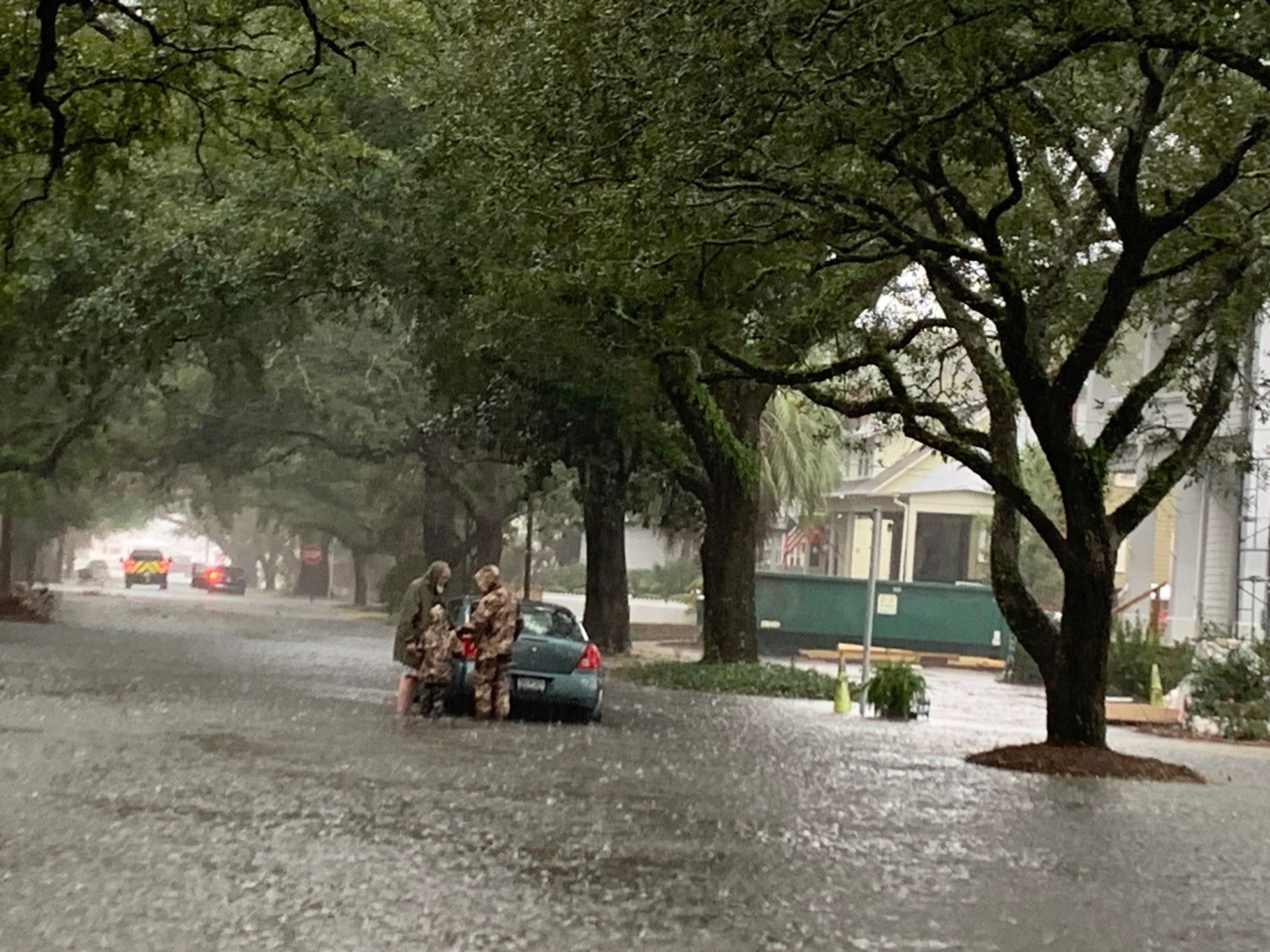 Three people surround a car on a flooded street.