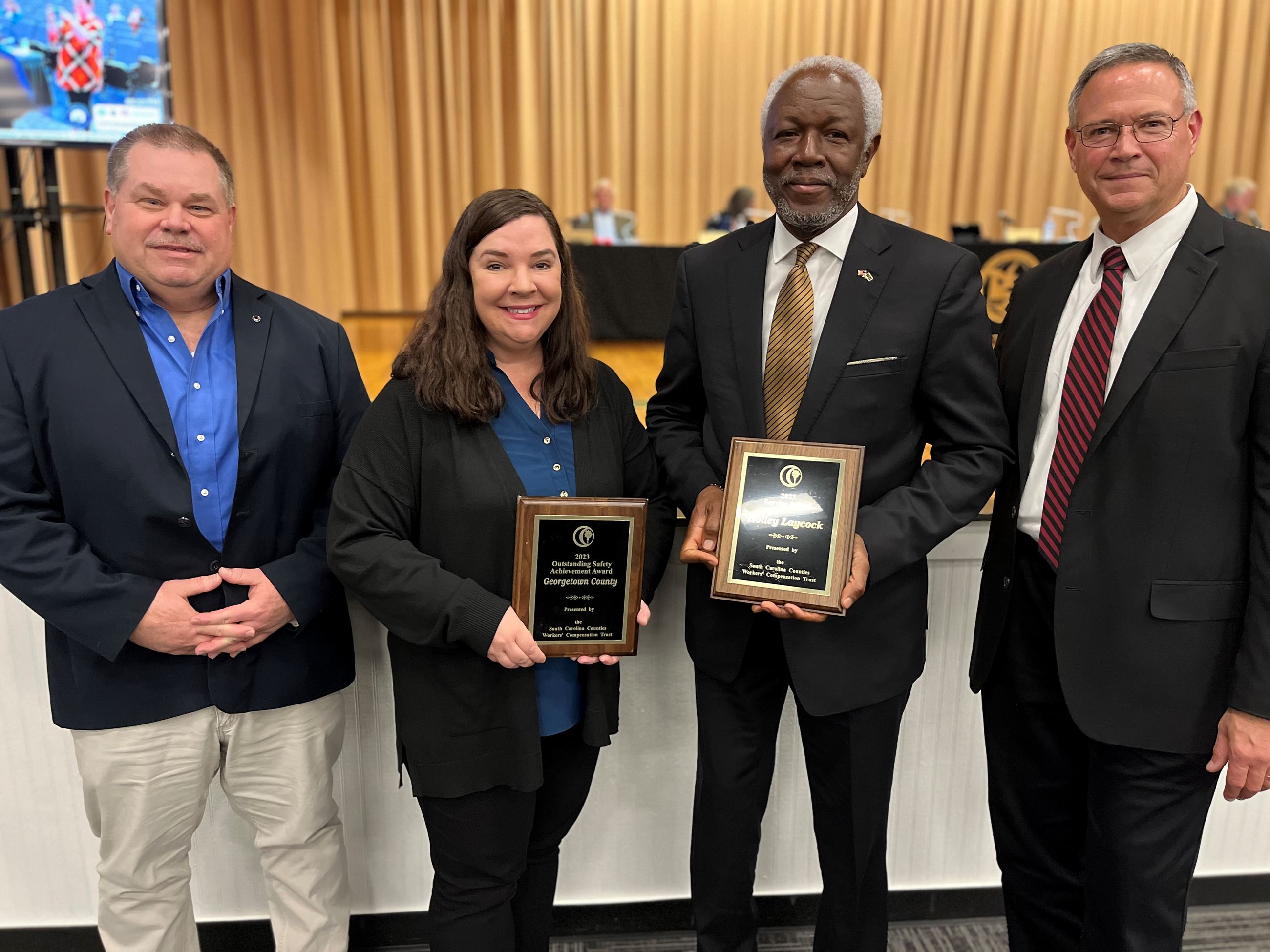 three men and a woman standing in front of a stage holding award plaques