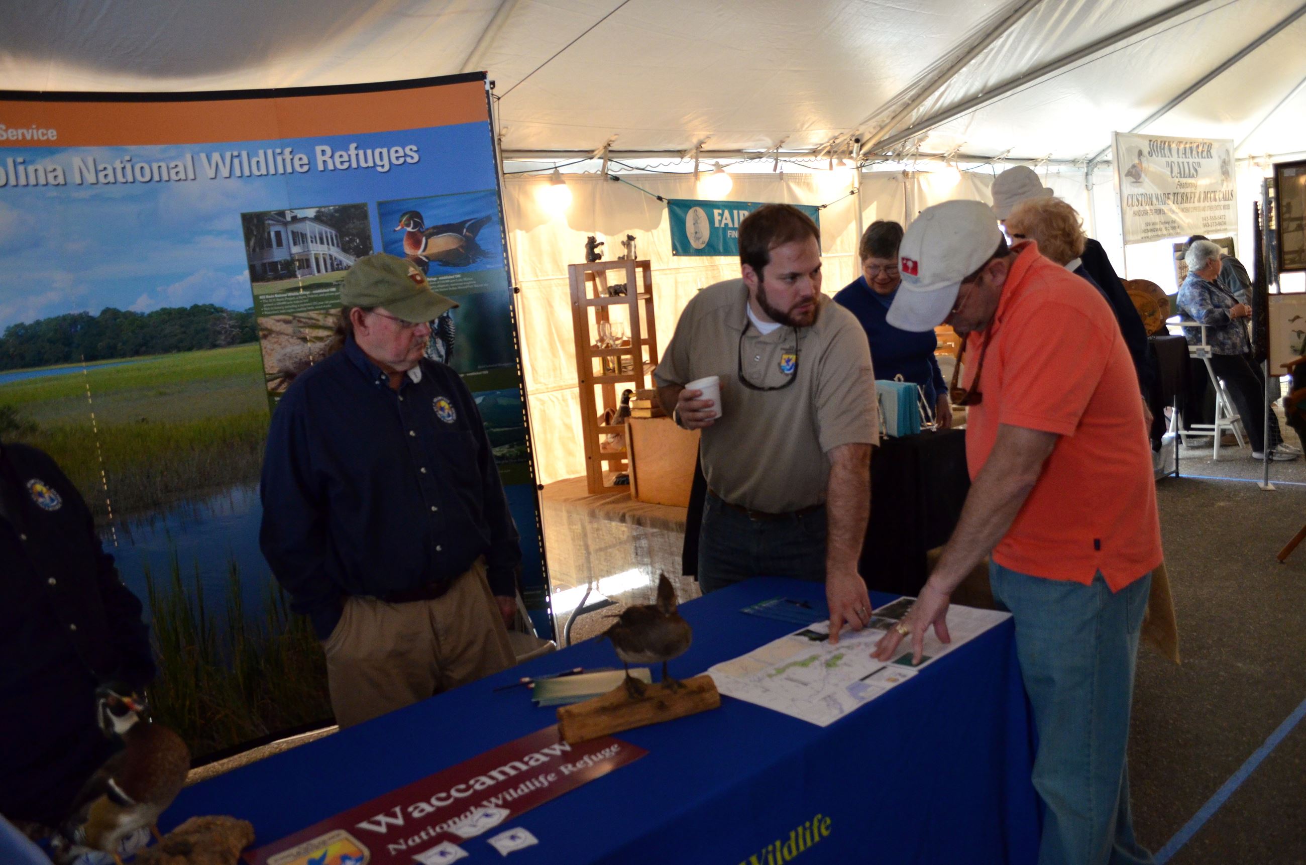 three people standing around a nature-themed informational display under a tent