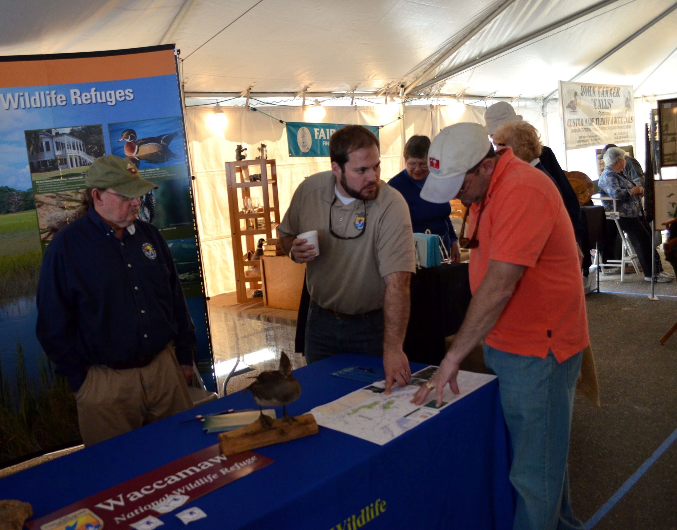 three people standing around a nature-themed informational display under a tent