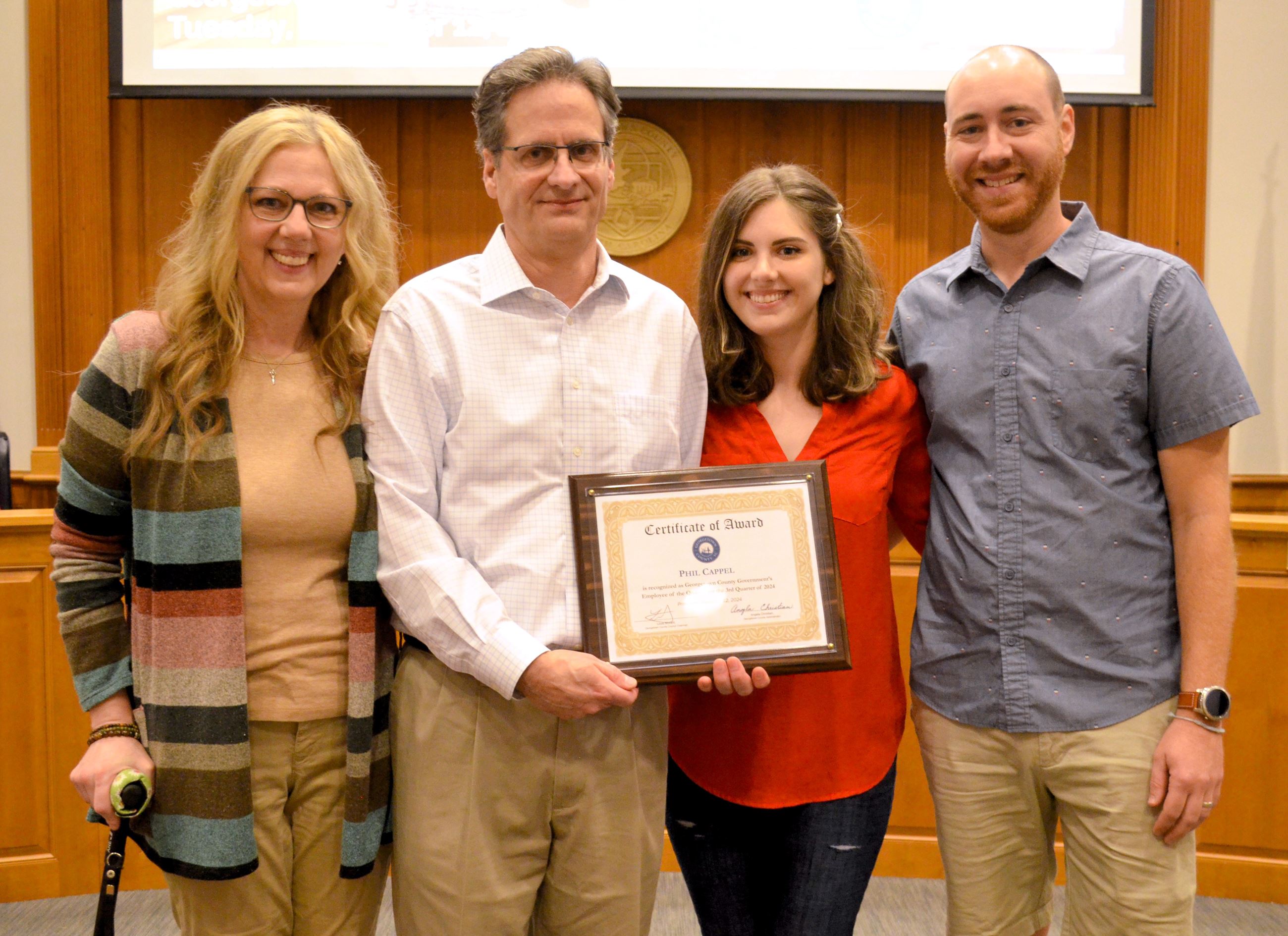 Phil Cappel holding a plaque and standing with his family.