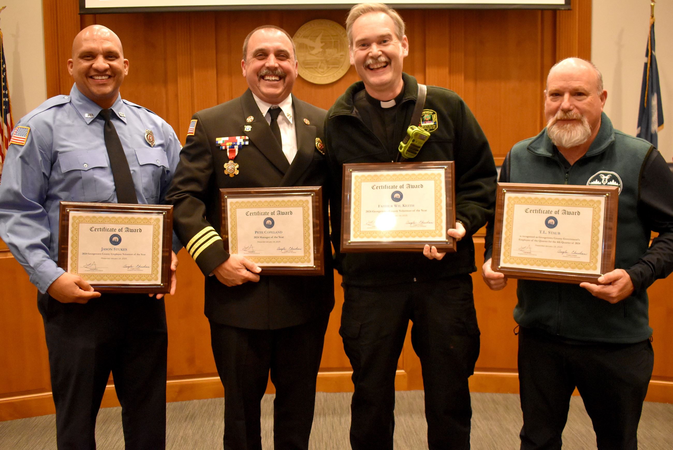 four smiling men lined up and holding plaques