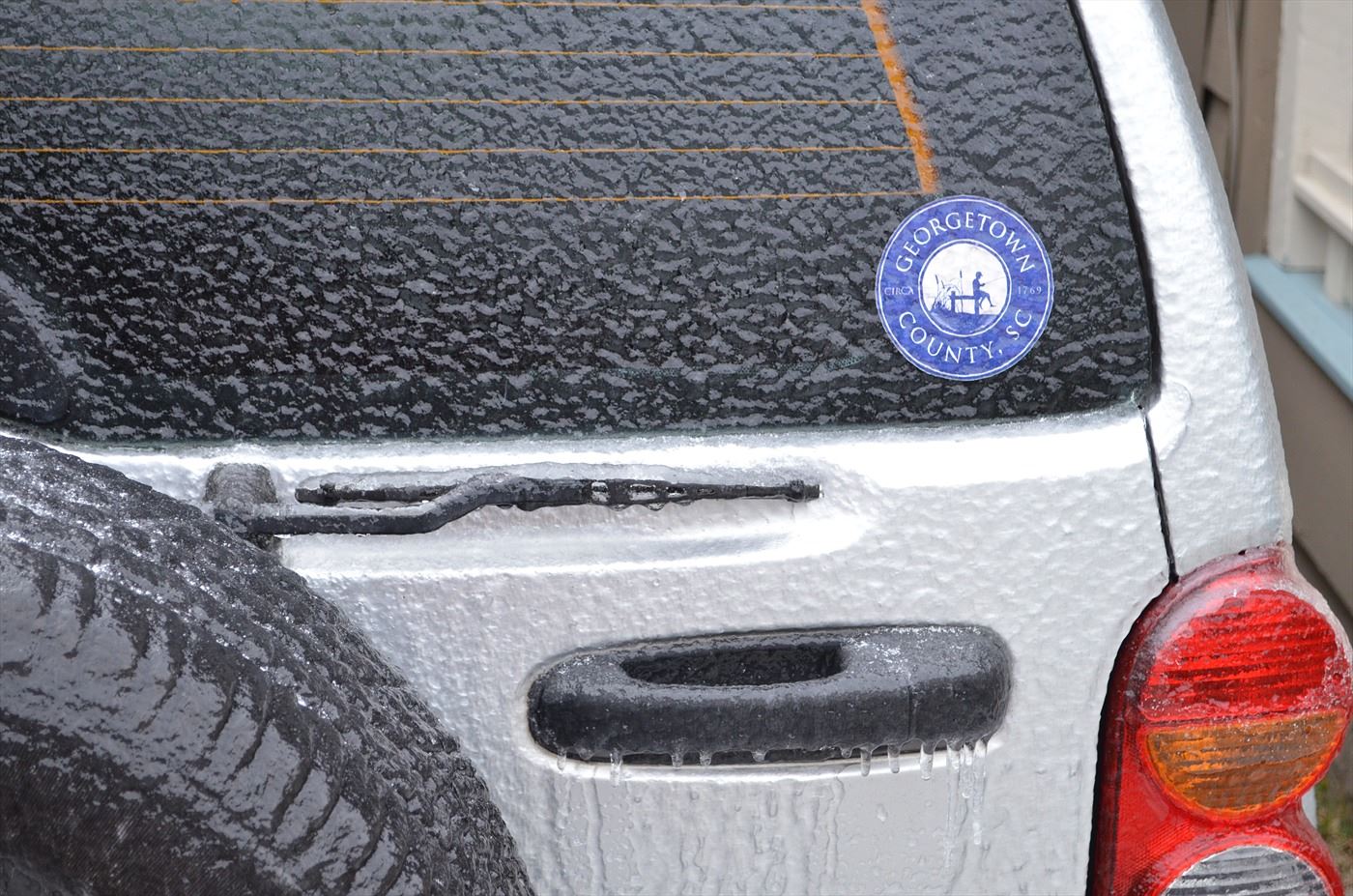 Ice covers the liftgate of a Jeep with a round Georgetown County sticker affixed to the glass
