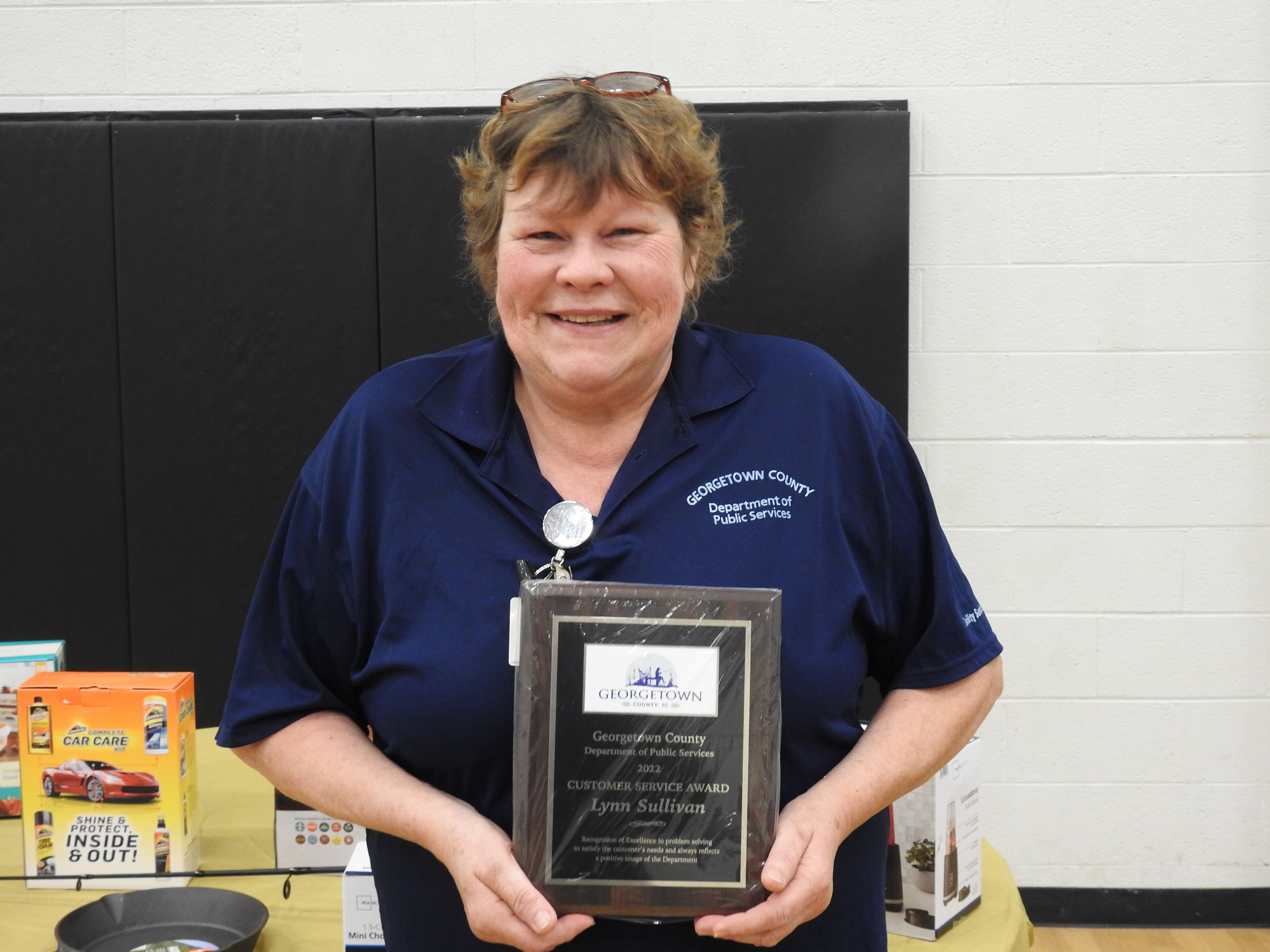 Woman wearing a navy blue shirt holding an award plaque and smiling.