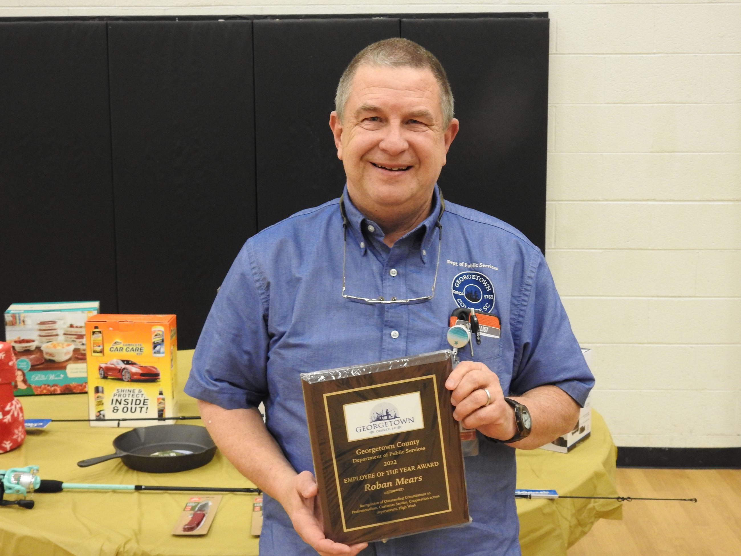 Man wearing a blue button-down, short-sleeved shirt holding an award plaque and smiling.